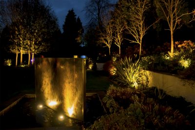 A lit water feature and garden beyond